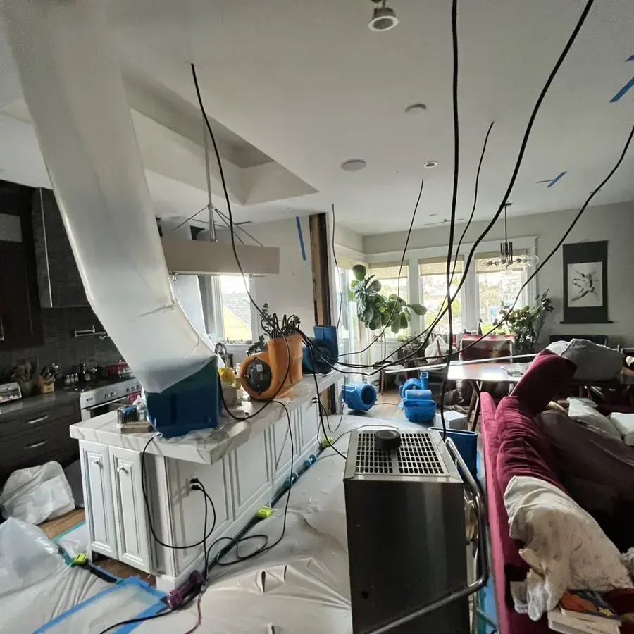 Drying ducts and air movers running through a kitchen and living area after a water leak