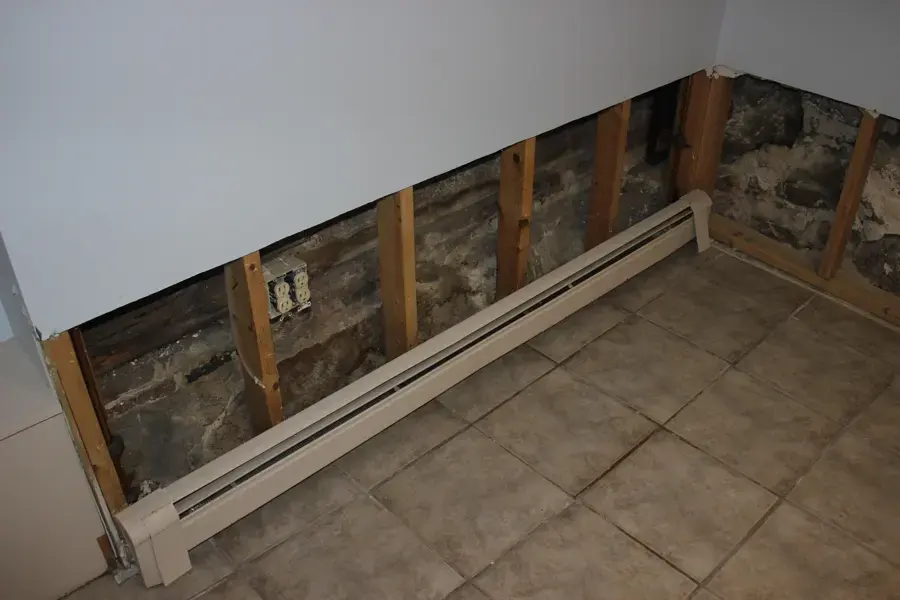 Drywall cut away along a wall above a baseboard heater during structural drying