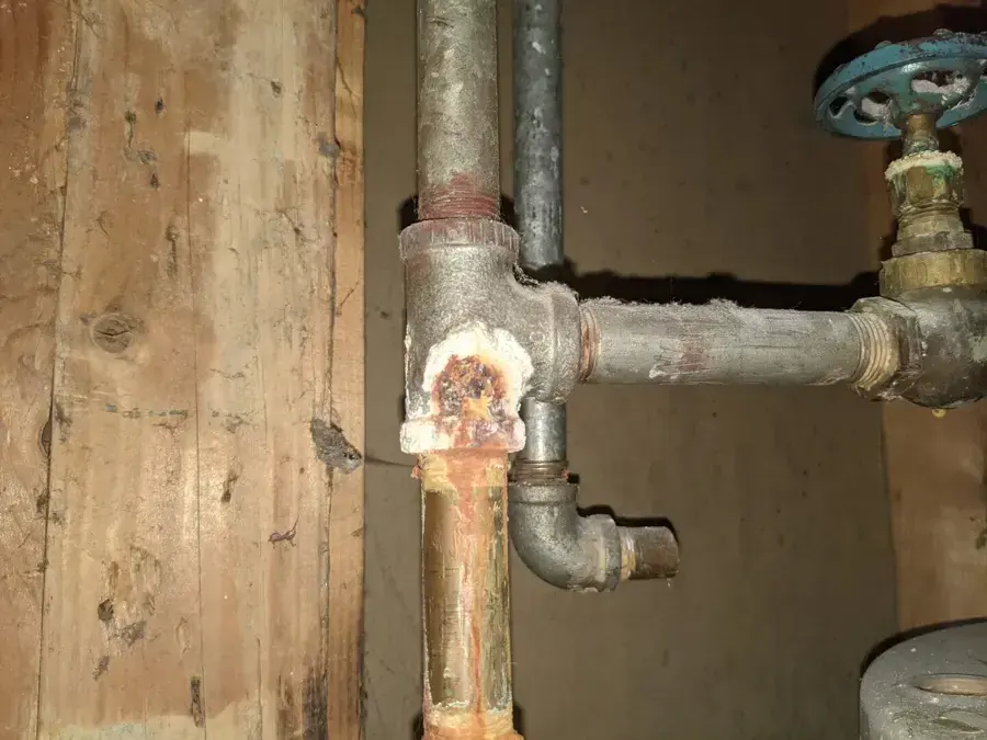 Corroded galvanized supply pipe fitting with mineral crust beside a shutoff valve