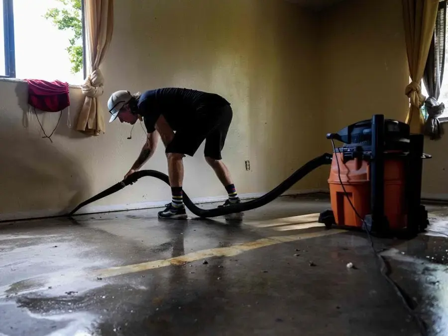 Technician extracting standing water from a concrete floor with a wet vacuum hose