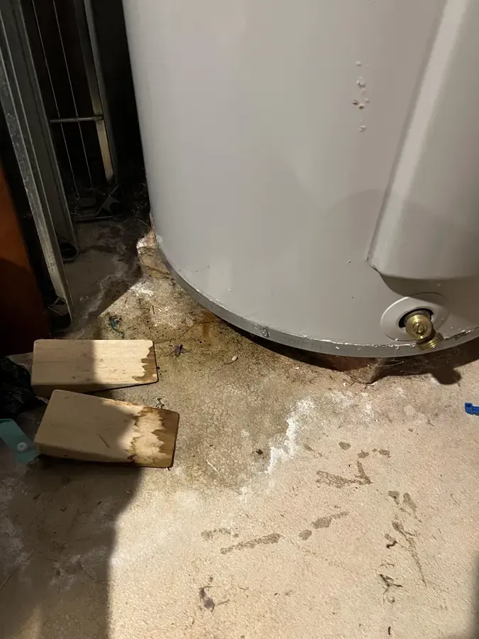 Tank water heater on a wet concrete floor with water spread around its base